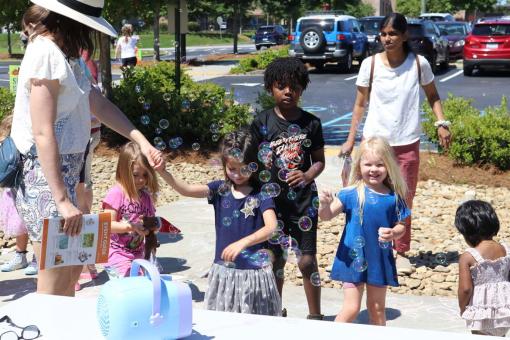 A group of children and adults enjoying an outdoor community bubble event on a sunny day