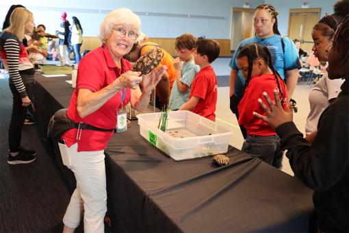 An interactive educational reptile presentation where a presenter holds a turtle shell for a group of children and adults